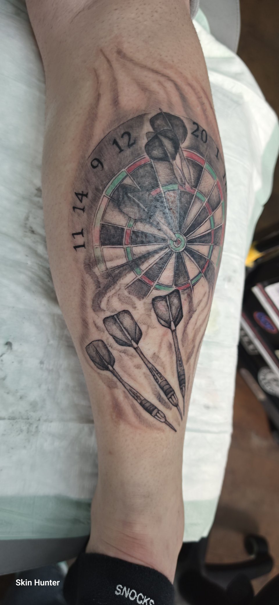 Realistic-Tattoo einer Dartscheibe mit Pfeilen an der Wade in Schwarz-Grau