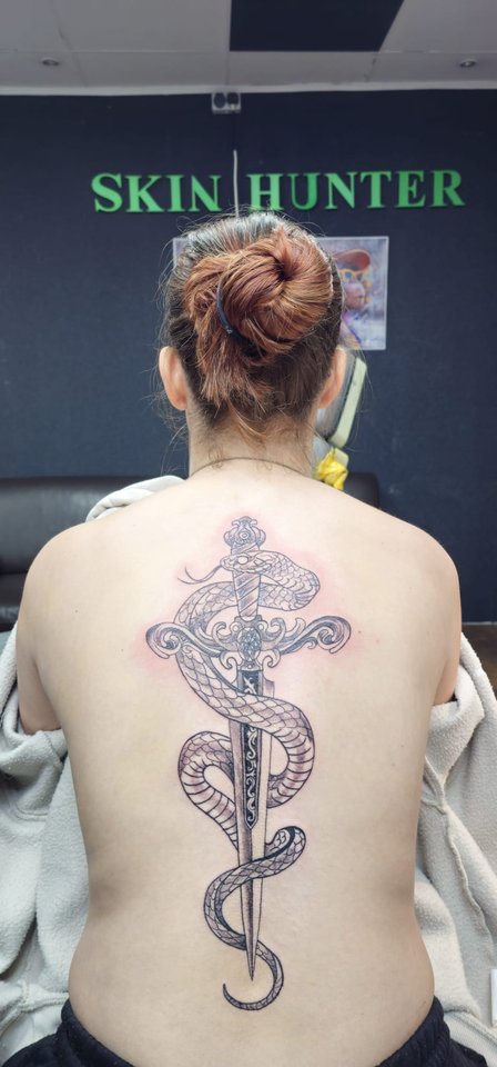 Frisch gestochene Schlange mit Dolch entlang der Wirbelsäule, im Hintergrund der Skin-Hunter-Schriftzug im Studio